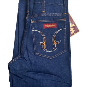 May include: A pair of dark blue denim jeans with a Wrangler label on the back pocket. The pocket has a decorative orange and white embroidery design.