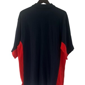 K&ouml;nnte beinhalten: Ein marineblaues Poloshirt mit roten Seitenteilen. Das Shirt hat kurze &Auml;rmel und einen Kragen.