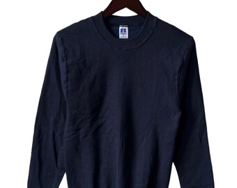 May include: A navy blue sweatshirt with a crew neck and long sleeves. The sweatshirt has a small red, white, and blue logo on the left chest and a tag on the right sleeve.