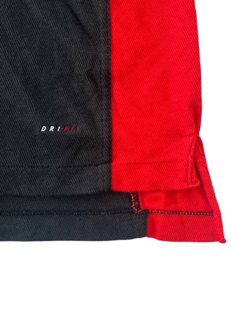 K&ouml;nnte beinhalten: Schwarz-rotes Sport-Shirt mit Dri-FIT-Logo. Das Shirt hat eine schwarze Seitenpartie und eine rote Seitenpartie.