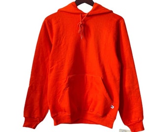 May include: A bright orange hooded sweatshirt with a kangaroo pocket and a Russell Athletic brand tag. The sweatshirt is hanging on a wooden hanger.