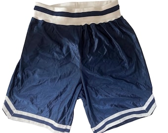 May include: Navy blue athletic shorts with white stripes along the hem and waistband. The waistband is a wide band of white fabric with two navy blue stripes. The shorts are made of a shiny, silky material.