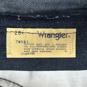 May include: A yellow care label with the text "Wrangler" and instructions for washing the jeans. The label also includes the size "28" and the number "7M561".