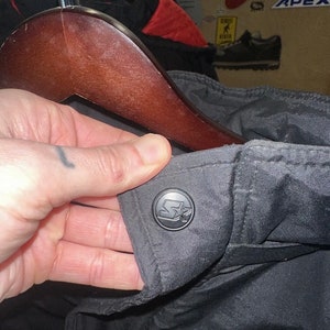 May include: Black jacket with a Starter logo button. The jacket is hanging on a wooden hanger. The Starter logo is a black circle with a white star and the letter "S".
