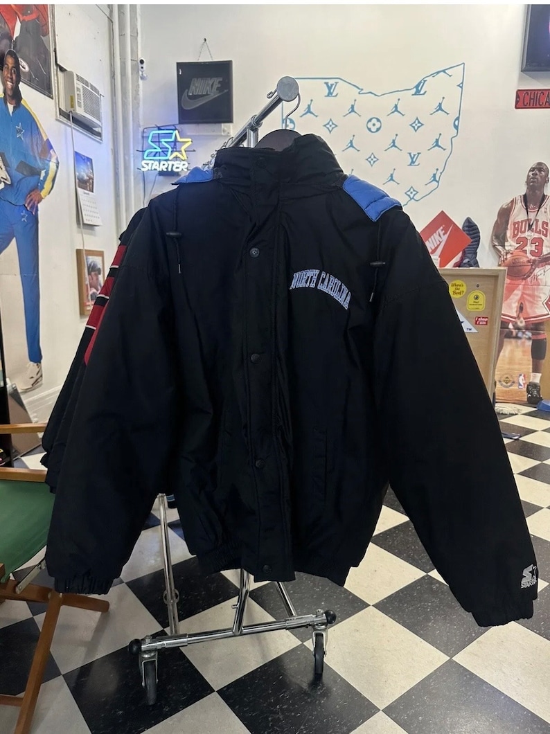 May include: Black North Carolina jacket with blue hood detailing. The jacket features a button-up front and the words "North Carolina" are embroidered across the chest. The Starter logo is visible on the sleeve.