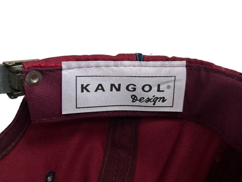 May include: A burgundy baseball cap with a white label that reads "Kangol Design" in black lettering.