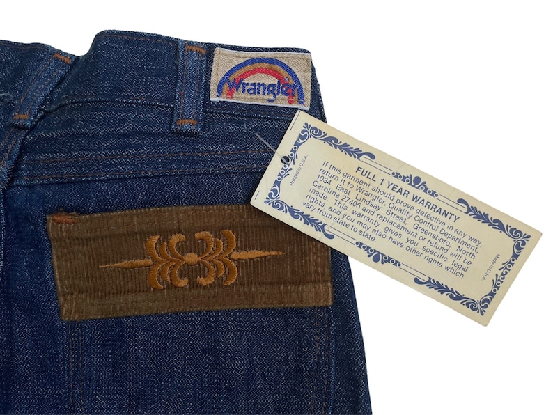 May include: Blue denim jeans with a brown corduroy patch on the back pocket. The patch has an embroidered design. A white tag with the text "FULL 1 YEAR WARRANTY" is attached to the jeans.
