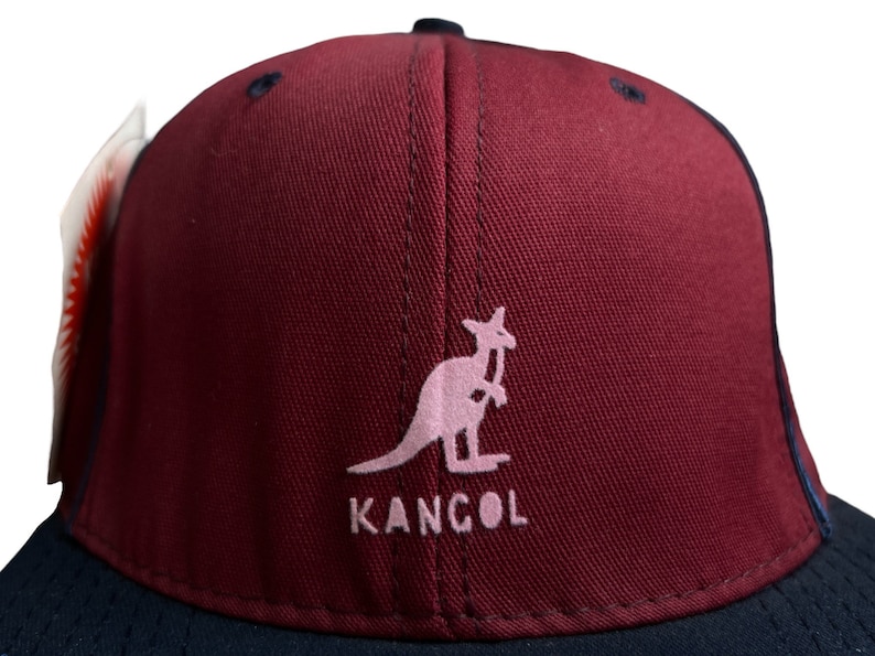 May include: A burgundy baseball cap with a black brim. The front of the cap features a pink kangaroo logo with the word "KANGOL" underneath.