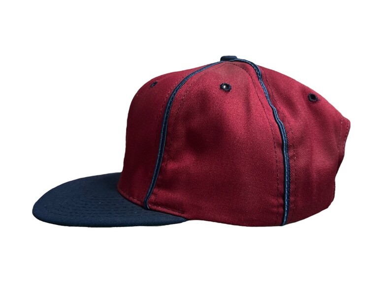 May include: A maroon baseball cap with a navy blue brim and a navy blue stitching detail around the crown.