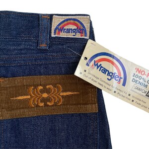 May include: A pair of blue denim jeans with a brown corduroy patch on the back pocket. The patch has an embroidered design. The jeans have a Wrangler label on the back waistband. The label says "Wrangler" and has a rainbow design. A tag attached to the jeans says "NO-FAULT" 100% COTTON DENIM WITH -SANFOR SET. Shrinkage Controlled for Perfect Fit Wrinkle-free Out of dryer ready to wear Pucker-free Fade great.