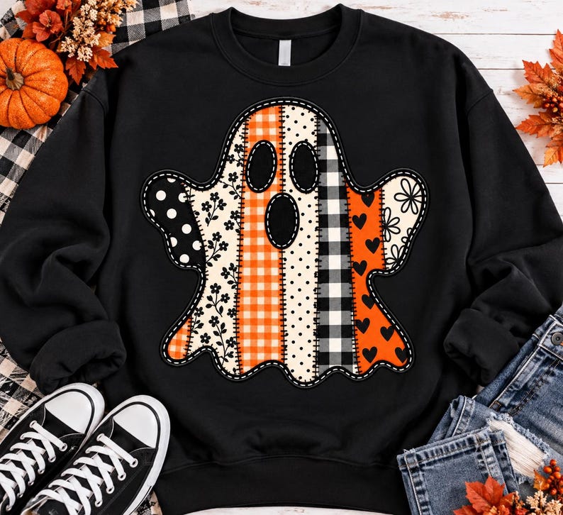 Puede incluir: Una sudadera negra de manga larga con un gran gr&aacute;fico de fantasma en el centro. El fantasma est&aacute; compuesto por paneles verticales de patchwork con varios patrones, incluyendo cuadros vichy naranjas, lunares blancos y negros, flores y corazones.