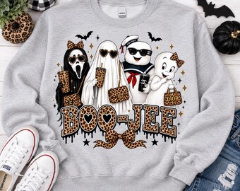 May include: A light gray crewneck sweatshirt featuring a graphic of four cartoon ghosts wearing leopard print accessories and sunglasses. The text BOO-JEE is printed in a leopard print font below the characters, accompanied by small stars and bats.