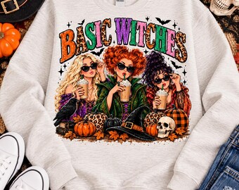 Puede incluir: Una sudadera gris claro de cuello redondo con un estampado gráfico que incluye el texto BASIC WITCHES. El diseño muestra tres figuras con gafas de sol sosteniendo tazas de café, rodeadas de calabazas, un cuervo negro, una calavera y un sombrero de bruja.
