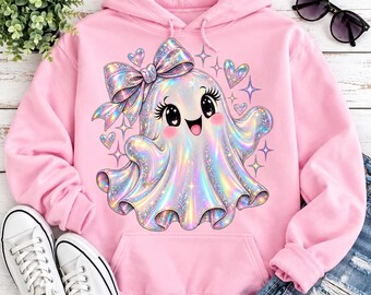 Puede incluir: Una sudadera con capucha de color rosa claro que presenta un gráfico central de un fantasma holográfico y brillante con un lazo grande, pestañas largas y una expresión sonriente, rodeado de pequeñas estrellas y corazones.