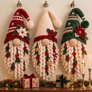 May include: Three hanging crochet gnome decorations with pointed hats in red, cream, and green. Each gnome features a textured cream beard adorned with small pinecones, red berries, and greenery. The hats are topped with pom-poms and floral accents.