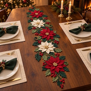 May include: A crochet table runner featuring red and white poinsettia flowers with green holly leaves and small red berries. The runner is centred on a wooden dining table set with white plates, dark green napkins, and gold-toned cutlery.