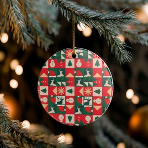 May include: A round ceramic ornament featuring a repeating grid pattern of red, green, and cream squares. The design includes silhouettes of reindeer, snowmen, Christmas trees, Santa hats, and starburst shapes. A gold string hangs from the top.