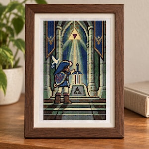 Puede incluir: Un bordado en punto de cruz enmarcado que representa a un personaje pixelado con túnica azul frente a una espada incrustada en un pedestal de piedra bajo un arco, con un símbolo de triángulo dorado brillante y estandartes azules.