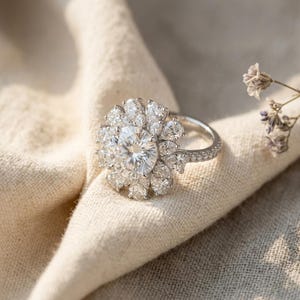 May include: A silver-toned ring featuring a large, round, brilliant-cut center stone surrounded by a halo of multiple pear-shaped stones arranged in a floral pattern. The band is thin and encrusted with small, round, sparkling white stones.