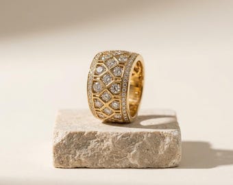 May include: A wide gold band ring featuring a central lattice pattern filled with round brilliant cut diamonds. The edges of the ring are lined with smaller pavé set diamonds, creating a textured, reflective surface across the entire gold band.