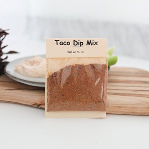 May include: A small, clear plastic bag filled with a red and brown spice mix. The bag has a label that reads "Taco Dip Mix" and "Net wt 1/4 oz".