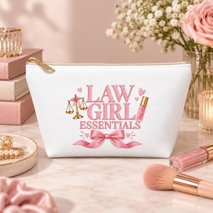 May include: A white zippered pouch featuring a pink graphic design with the text "LAW GIRL ESSENTIALS," a gold scale of justice icon, a pink lip gloss illustration, and a large pink ribbon bow at the bottom, accented with small pink hearts.