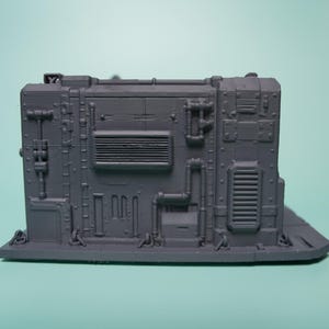 May include: A matte grey 3D printed miniature terrain piece featuring a rectangular industrial wall section. The surface is detailed with raised pipes, vents, rivets, and paneling, creating a textured, mechanical appearance for tabletop gaming.