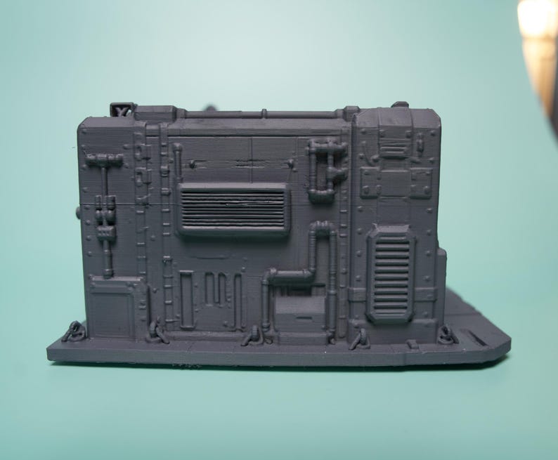 May include: A matte grey 3D printed miniature terrain piece featuring a rectangular industrial wall section. The surface is detailed with raised pipes, vents, rivets, and paneling, creating a textured, mechanical appearance for tabletop gaming.