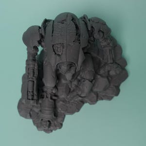 May include: A dark gray, 3D-printed miniature robot figure in a kneeling position, featuring intricate mechanical details, articulated limbs, and a textured armor plating surface, mounted on a rocky, uneven base with visible layer lines.