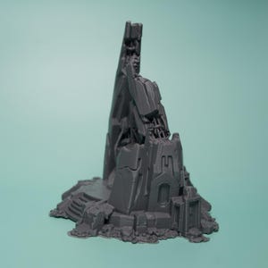 Może przedstawiać: Szary, niemalowany, wydrukowany w 3D miniaturowy element terenu przedstawiający wysoką, poszarpaną, futurystyczną iglicę wyrastającą ze skalistej, mechanicznej podstawy. Konstrukcja posiada złożone geometryczne panele oraz warstwy gruzu.