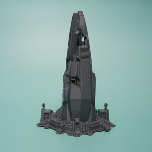 K&ouml;nnte beinhalten: Eine graue, 3D-gedruckte Miniaturstruktur mit einem hohen, gezackten, turmartigen Mittelteil, der geometrische Paneele und mechanische Details aufweist. Die Basis ist kreisf&ouml;rmig und von kleinen, symmetrischen architektonischen Elementen umgeben.