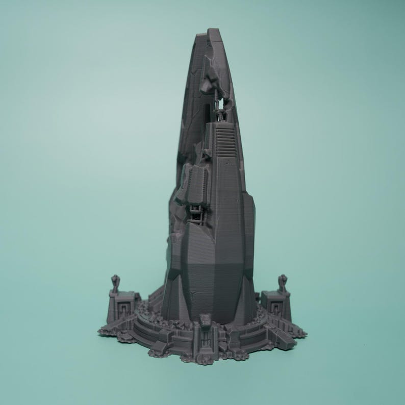 K&ouml;nnte beinhalten: Eine graue, 3D-gedruckte Miniaturstruktur mit einem hohen, gezackten, turmartigen Mittelteil, der geometrische Paneele und mechanische Details aufweist. Die Basis ist kreisf&ouml;rmig und von kleinen, symmetrischen architektonischen Elementen umgeben.