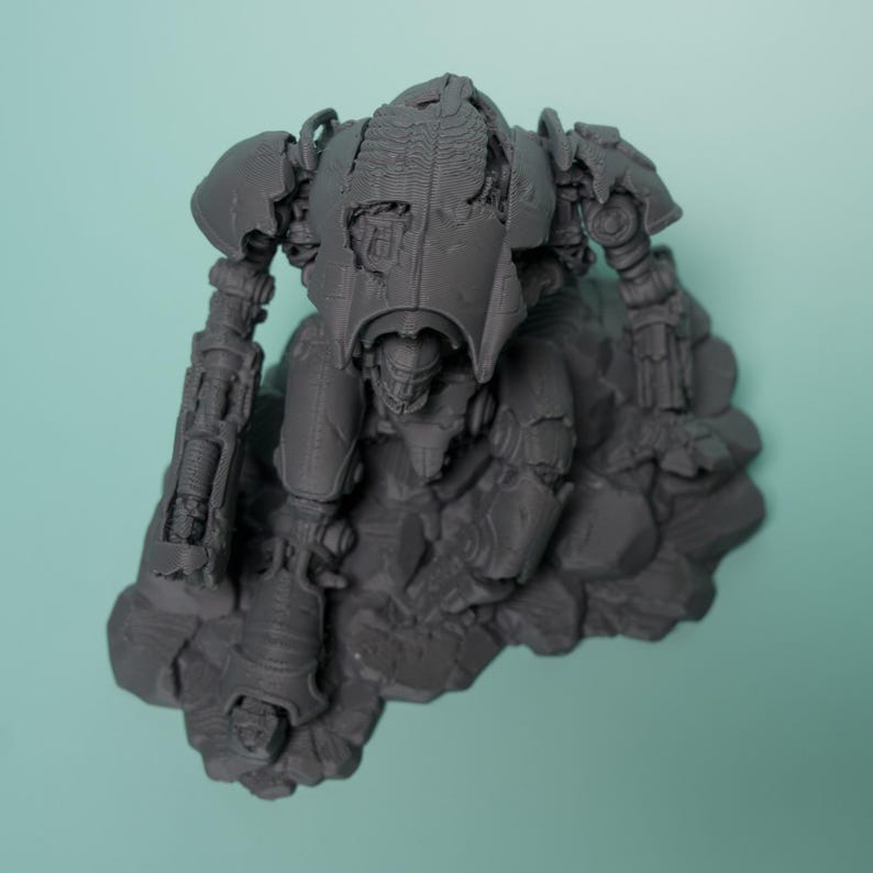 May include: A gray, unpainted resin miniature of a bipedal mechanical robot standing on a rocky, uneven base. The robot features intricate mechanical details, including articulated limbs, a central torso, and a damaged armor plating design.