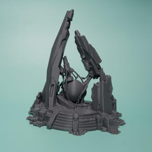 Może przedstawiać: Ciemnoszary, wydrukowany w 3D miniaturowy element terenu przedstawiający centralny sferyczny obiekt zamknięty w poszarpanych, zrujnowanych strukturach architektonicznych i gruzach, umieszczony na okrągłej podstawie ze schodkami i skalistym podłożem.