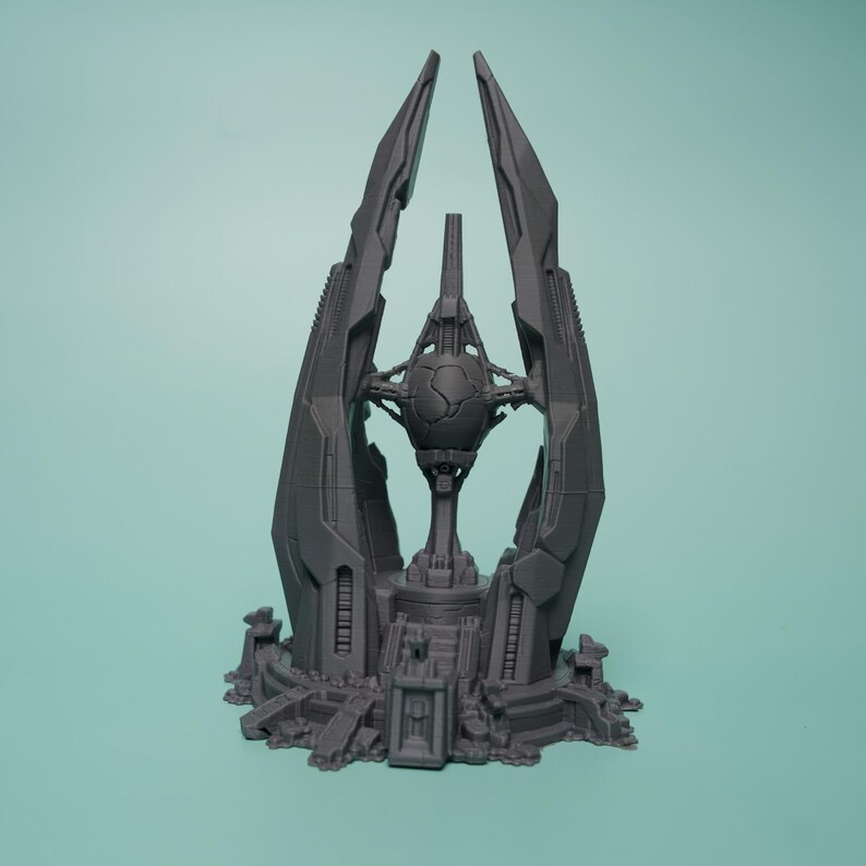 K&ouml;nnte beinhalten: Ein dunkelgraues, 3D-gedrucktes Miniatur-Gel&auml;ndest&uuml;ck mit einem zentralen kugelf&ouml;rmigen Kern, der in einer hohen, spitzen, mehrzinkigen Struktur aufgeh&auml;ngt ist. Die Basis ist kreisf&ouml;rmig mit komplizierten mechanischen Details und abgestuften Plattformen.