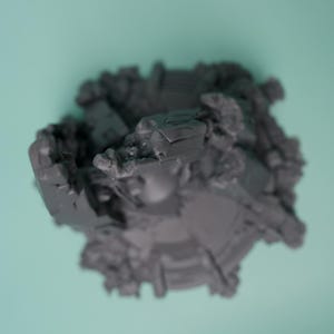 Może przedstawiać: Ciemnoszary, niepomalowany miniaturowy element terenu do gier z okrągłą podstawą, przedstawiający skomplikowane, poszarpane ruiny architektoniczne, gruz i odłamki rozrzucone wok&oacute;ł krawędzi, ujęty z perspektywy z g&oacute;ry.