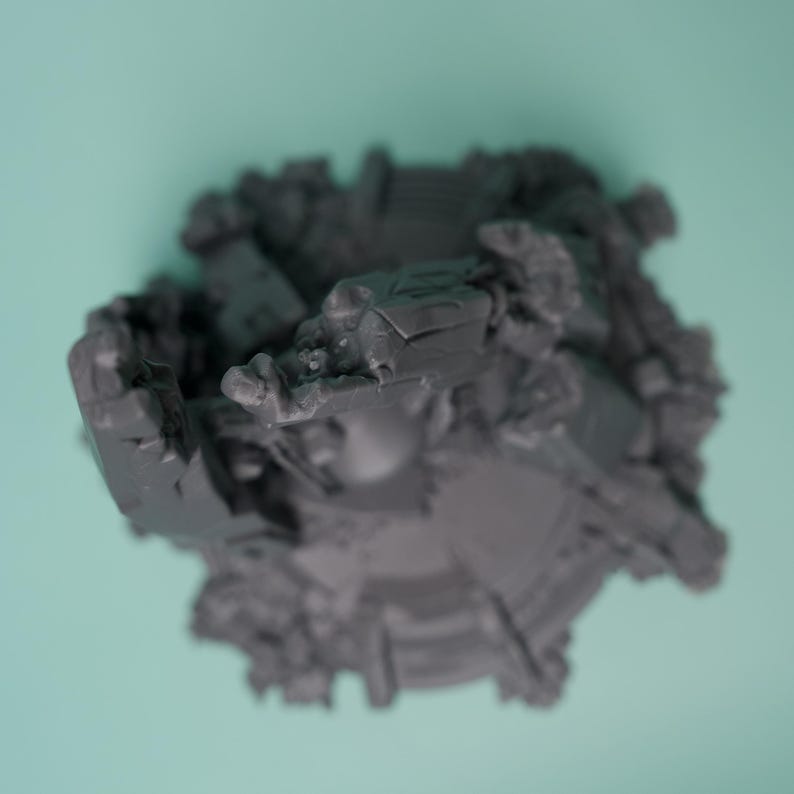 Może przedstawiać: Ciemnoszary, niepomalowany miniaturowy element terenu do gier z okrągłą podstawą, przedstawiający skomplikowane, poszarpane ruiny architektoniczne, gruz i odłamki rozrzucone wok&oacute;ł krawędzi, ujęty z perspektywy z g&oacute;ry.