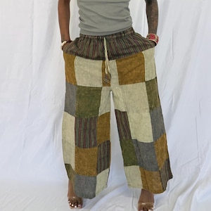 May include: Wide-leg patchwork trousers in brown, green, and beige. The design features a mix of striped and solid fabric squares. The waistband is striped with a drawstring. The trousers are worn by a person.