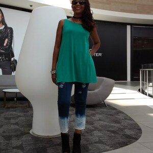 May include: A sleeveless, teal tunic top paired with distressed, dark wash jeans featuring a faded, ombre effect at the ankles. The outfit is completed with black ankle boots. The overall style is casual and modern.