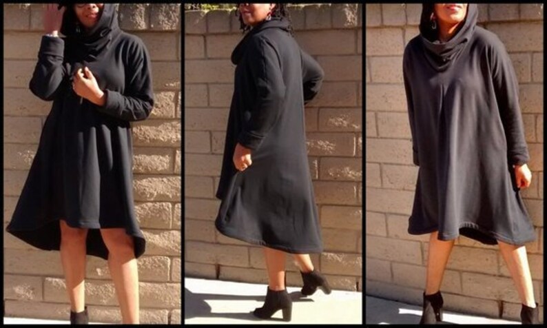 May include: A black hooded dress with long sleeves and a flared skirt. The dress has a cowl neck and is knee-length in the front, with a longer hem in the back. The model is wearing black ankle boots.