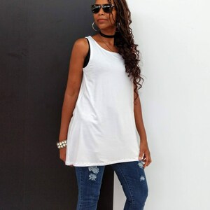 May include: A white sleeveless tunic top paired with distressed blue jeans. The top has a relaxed fit and a slightly asymmetrical hemline. The jeans feature ripped details at the knees.