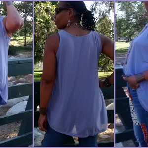 May include: A sleeveless, lilac-colored top with a flowing, asymmetrical hemline. The top is paired with blue jeans featuring decorative fabric patches in black, white, and orange. A red belt and long necklace complete the outfit.