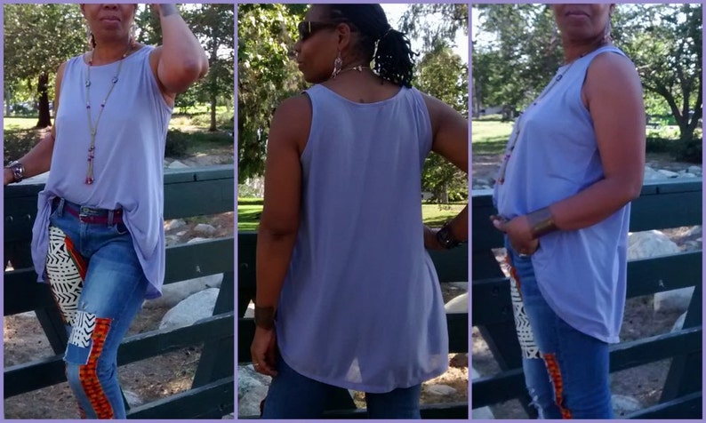 May include: A sleeveless, lilac-colored top with a flowing, asymmetrical hemline. The top is paired with blue jeans featuring decorative fabric patches in black, white, and orange. A red belt and long necklace complete the outfit.