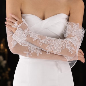 Peut inclure: Gants longs en tulle blanc transparent ornés de broderies florales blanches complexes et de détails en dentelle appliquée. Les gants dépassent les coudes et comportent une boucle pour le doigt afin de maintenir le tissu en dentelle en place.