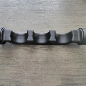 May include: A matte black, elongated, cylindrical object featuring a contoured, ergonomic grip with three distinct finger-shaped indentations along its length and two wider, circular end caps, designed for a secure hold during use.