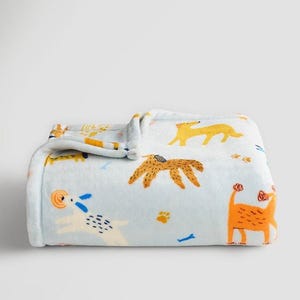 May include: A light blue fleece blanket featuring a repeating pattern of stylized dogs in shades of orange, yellow, and white. The design includes various dog breeds, small paw prints, and blue bones scattered across the soft, folded fabric surface.
