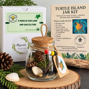 Peut inclure: Un kit en bocal en verre intitulé Turtle Island Jar Kit contenant du sable de rivage, des cendres, du feuillage naturel, une figurine de tortue, quatre perles, une plume décorative et de la ficelle, accompagné d'une boîte blanche et d'une carte.