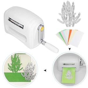 May include: A white manual die-cutting machine with a hand crank, a silver metal cactus-shaped cutting die, and a stack of multicolored paper sheets. The machine is shown feeding a green paper sheet through its rollers to create a cactus cutout.
