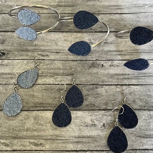 May include: A set of denim earrings and a denim bracelet. The earrings are teardrop shaped and the bracelet is a silver bangle with denim accents.