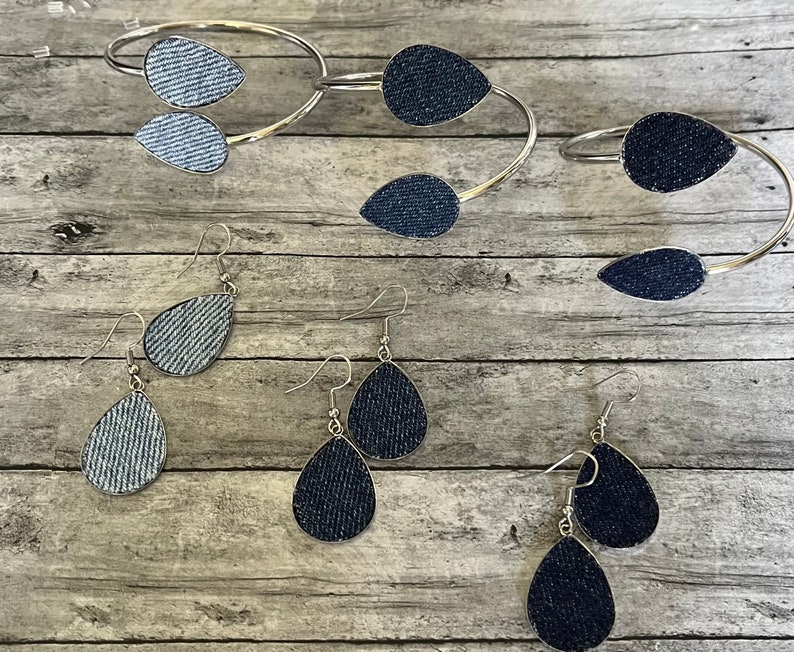 May include: A set of denim earrings and a denim bracelet. The earrings are teardrop shaped and the bracelet is a silver bangle with denim accents.